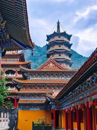A richly painted Chinese temple and pagoda set against forested hills